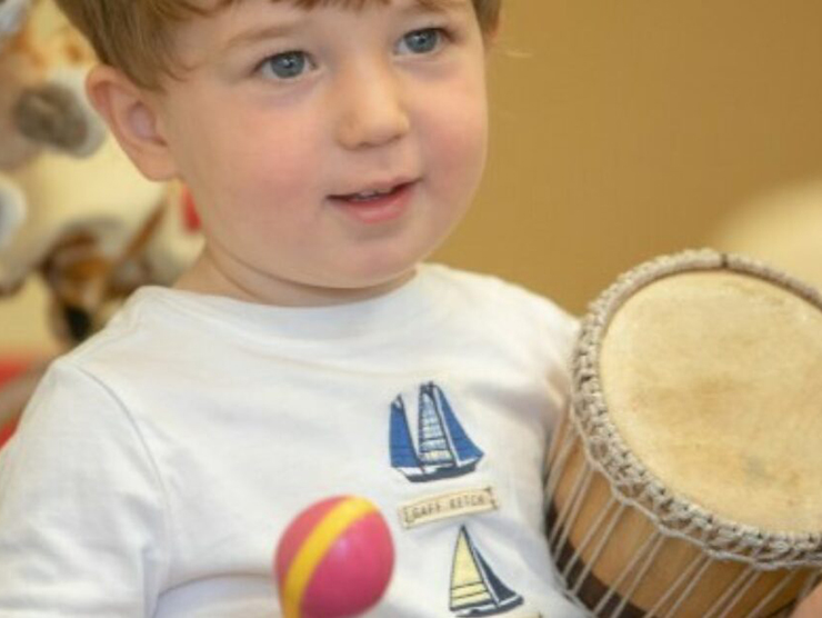 Toddler holding a drum and a maraca at Bright Horizons day care 